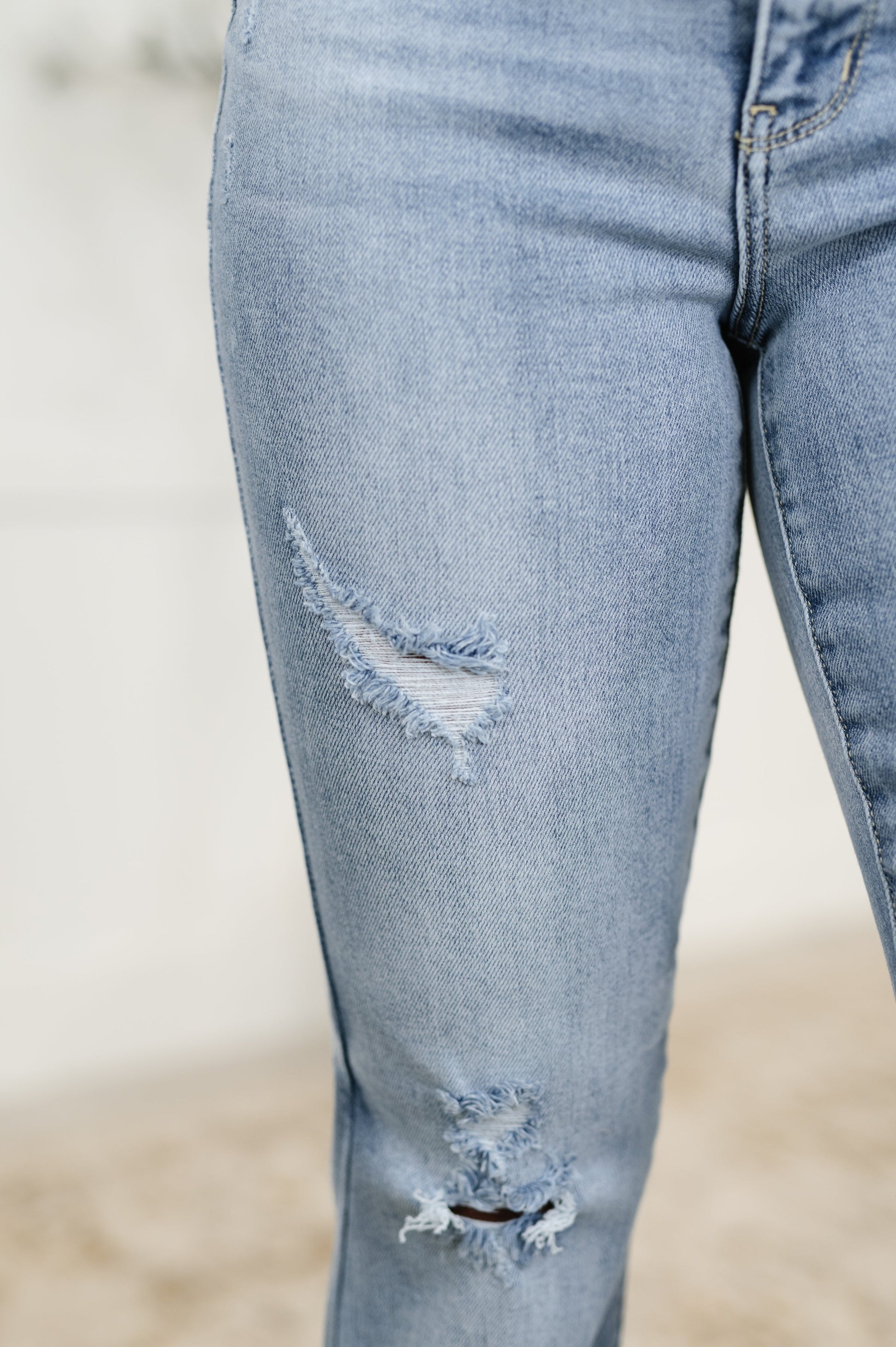 Close-up of light blue jeans with distressing details on a blurred background