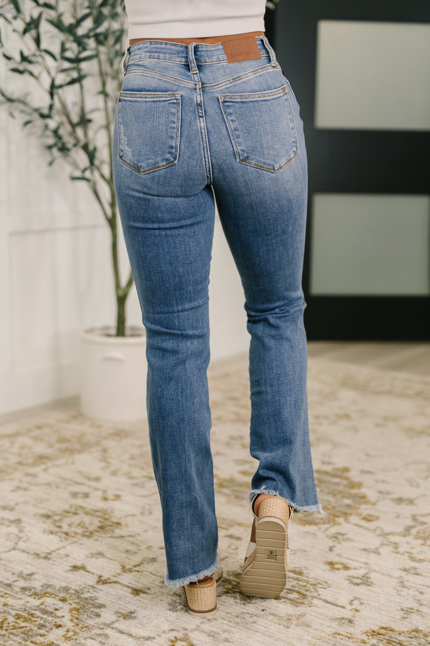 Person wearing blue jeans standing on a textured floor with a plant in the background