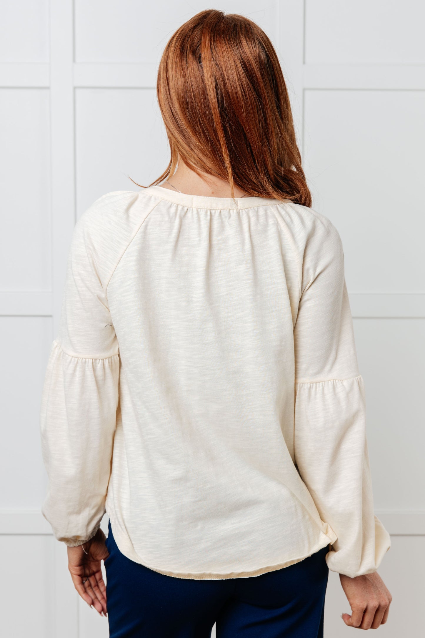 Woman wearing a white blouse with puffed sleeves against a light gray tiled wall.