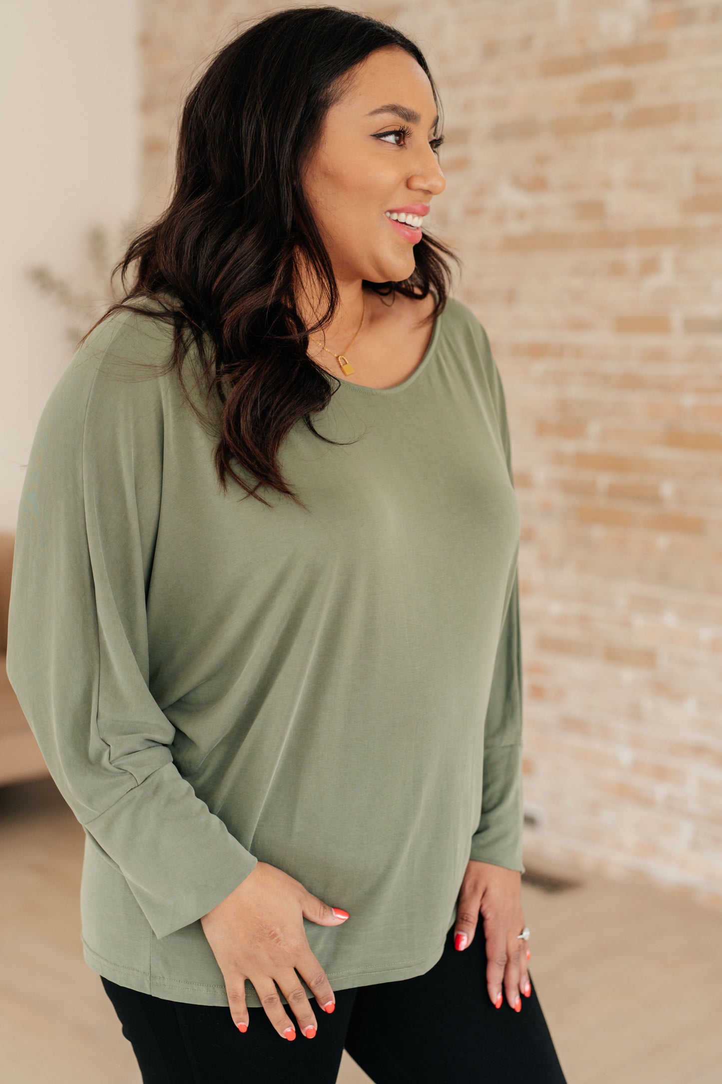 Woman wearing a green long-sleeve top with a brick wall background