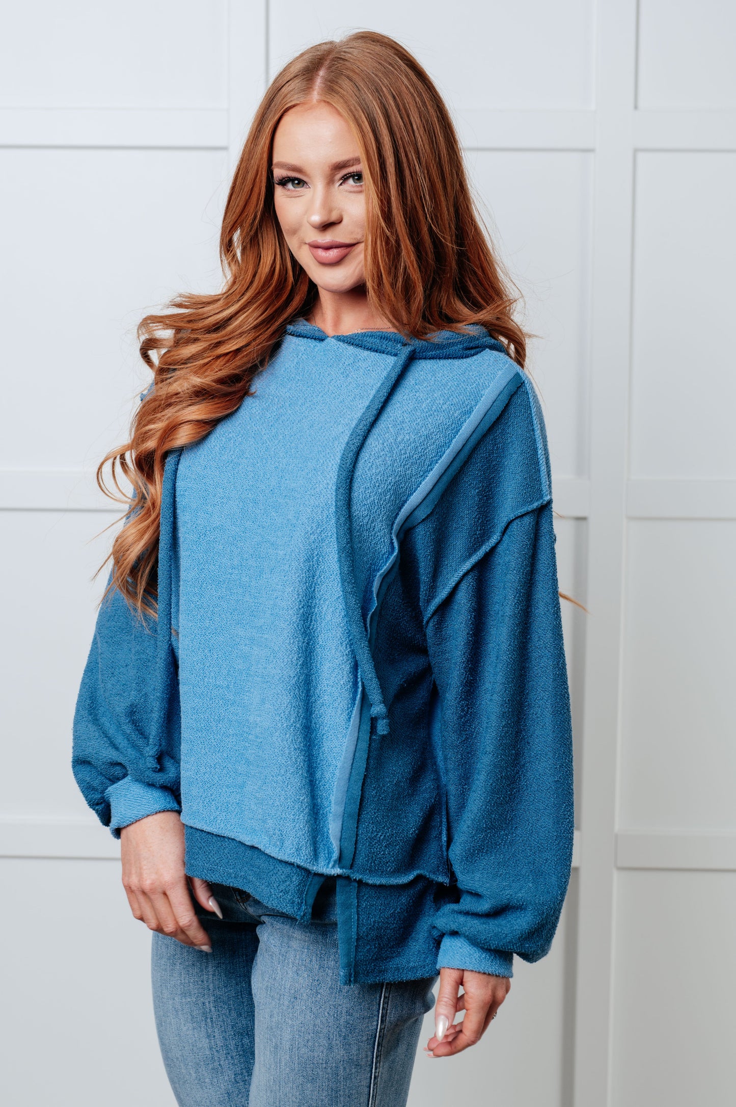 Woman wearing a blue hoodie against a white tiled wall