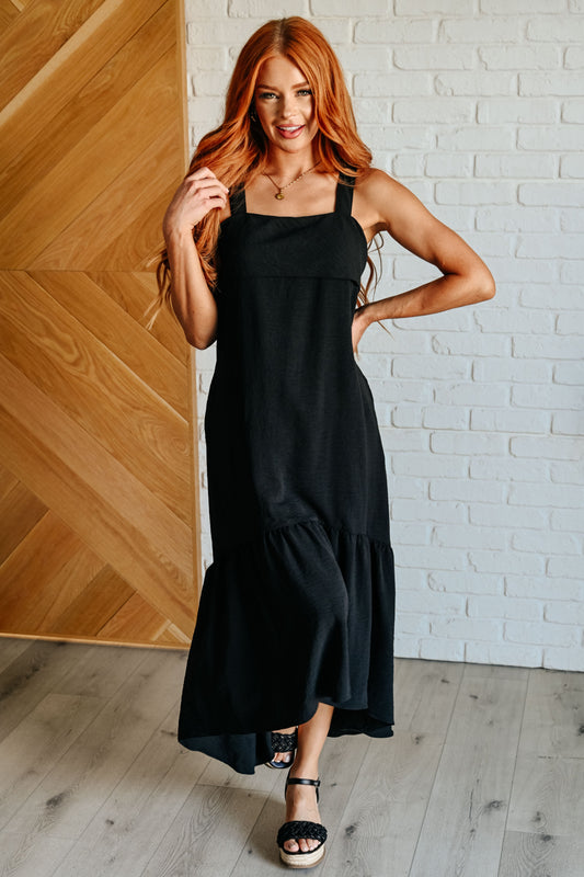 Woman in a black dress standing against a wooden wall and white brick wall.