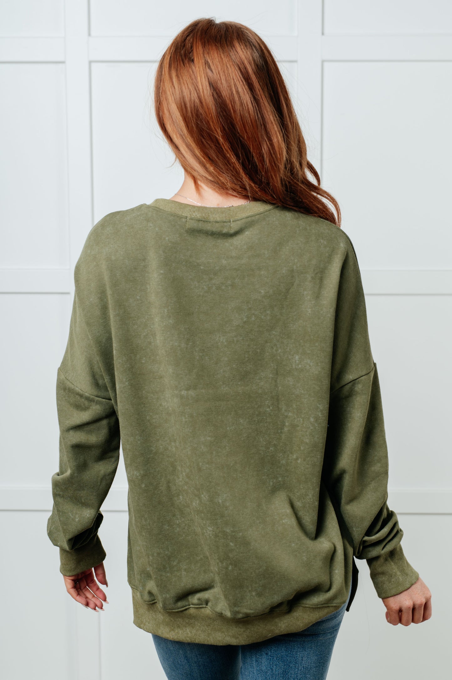 Person wearing an olive green sweatshirt against a white tiled wall