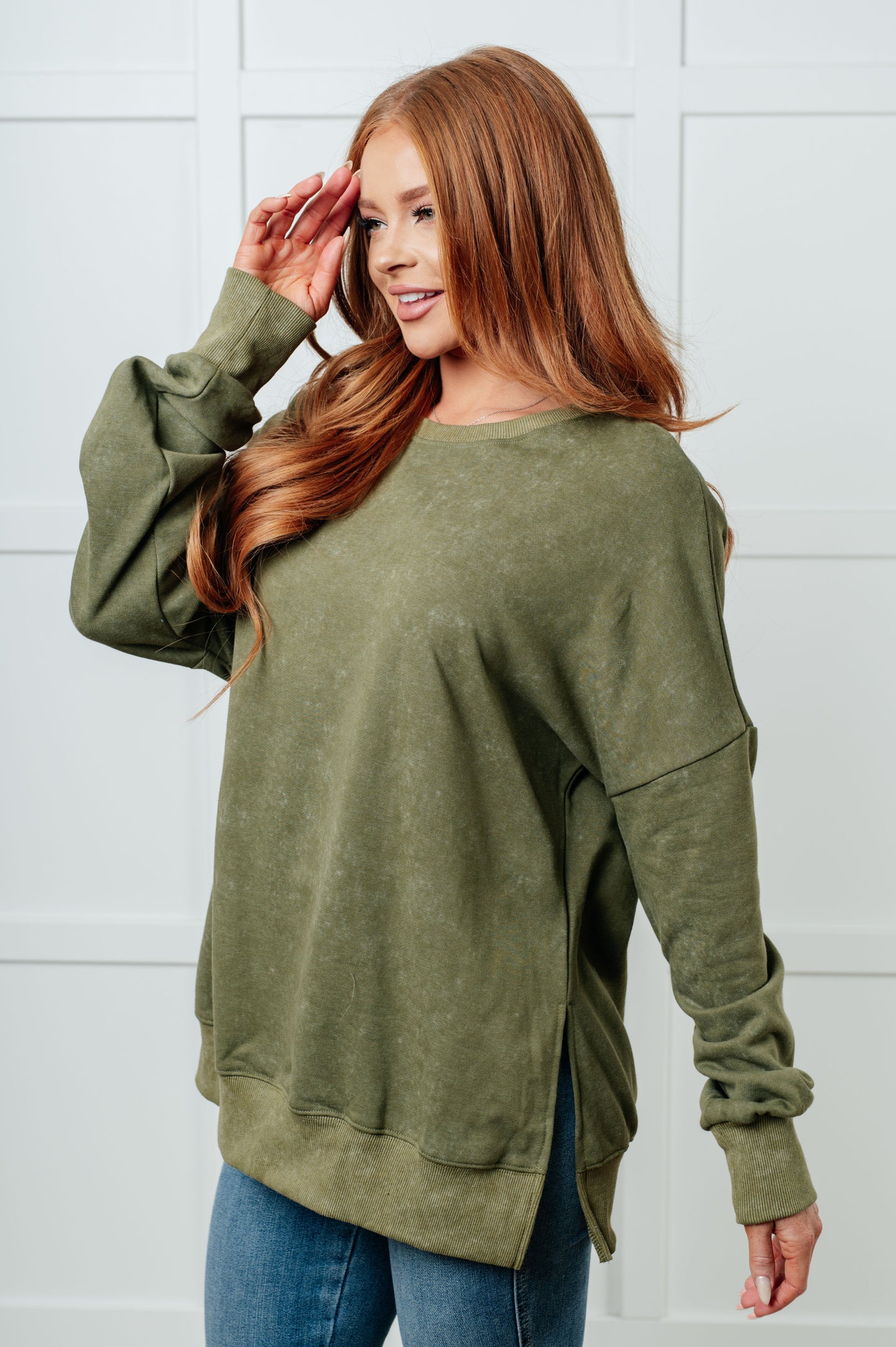 Woman wearing an olive green sweatshirt against a white wall