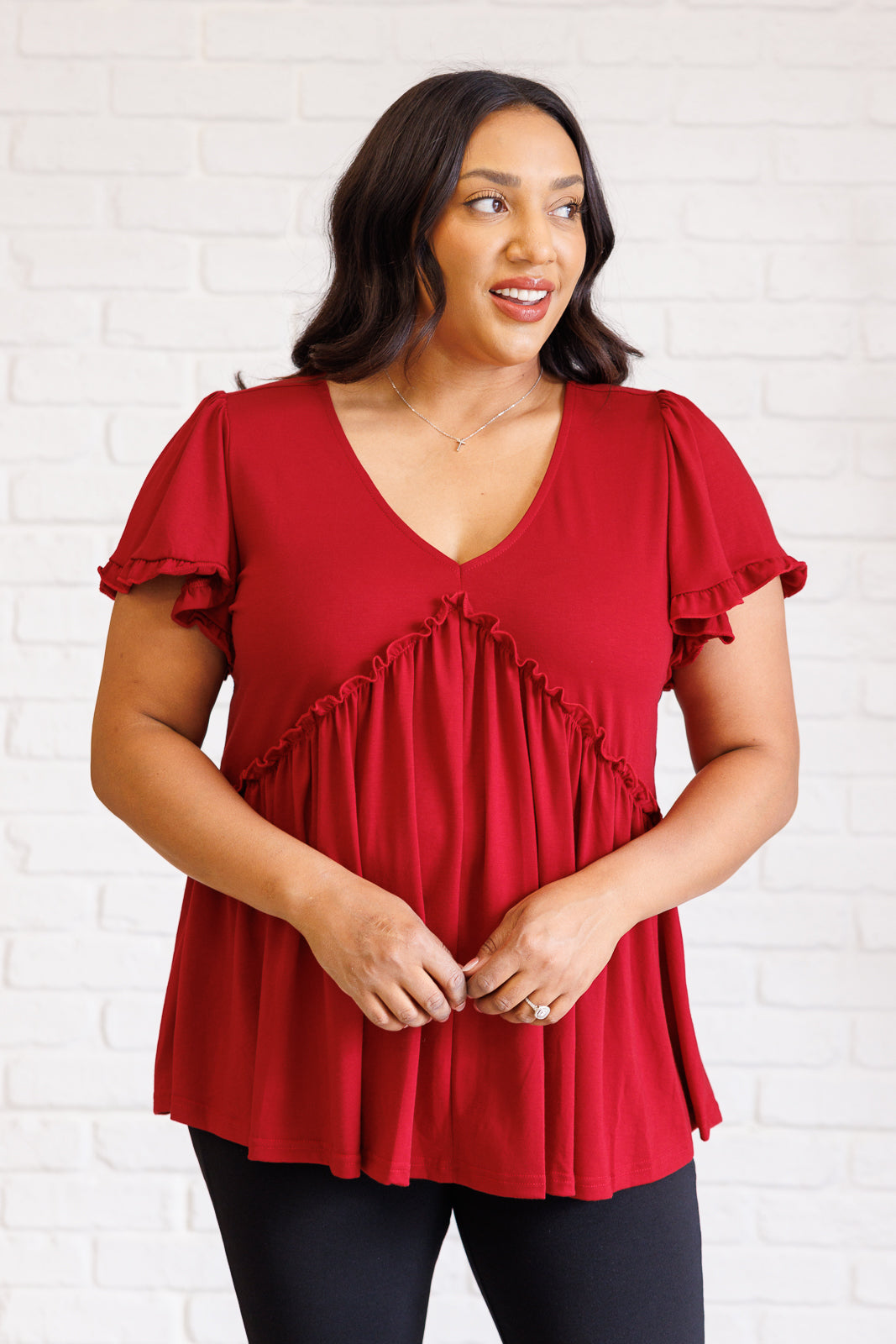 Woman wearing a red blouse with ruffled details against a white brick wall.