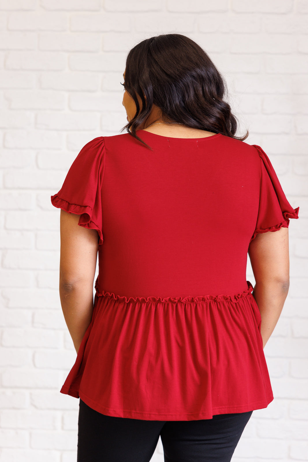 Red blouse with ruffled sleeves worn by a person against a white brick wall.