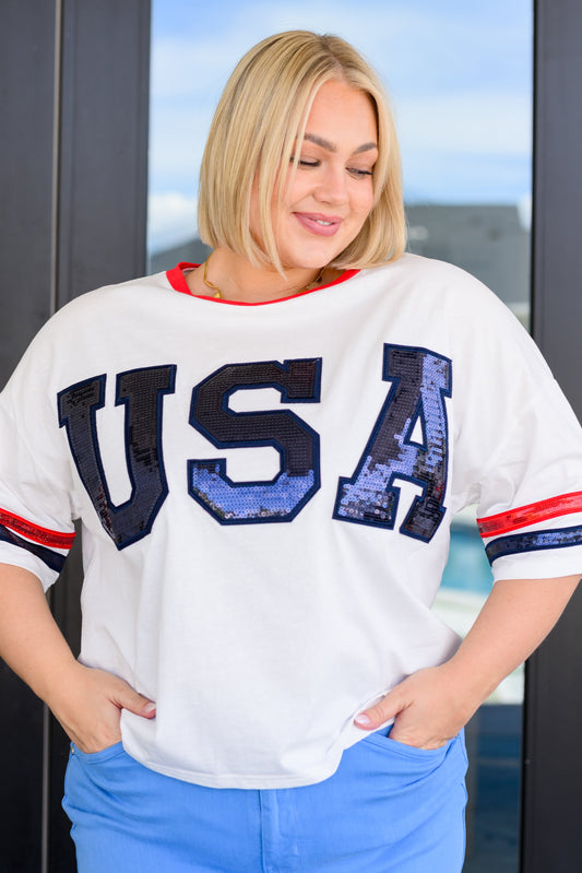 Woman wearing a white t-shirt with 'USA' printed on it, standing indoors.