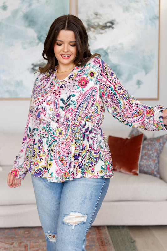 Woman wearing a colorful patterned blouse and jeans in a living room setting.