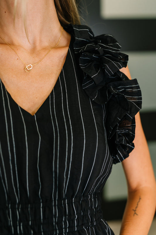 Black pinstripe dress with ruffled shoulders worn by a person.