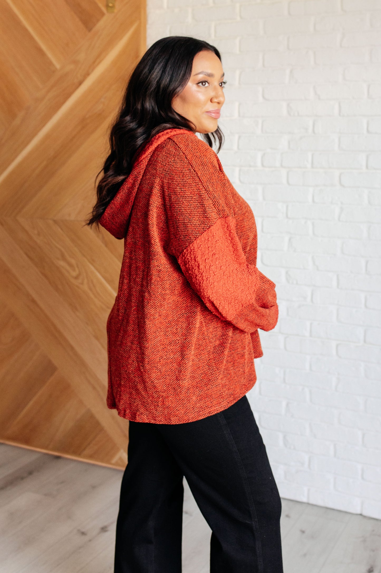 Woman wearing an orange sweater standing against a white brick wall.