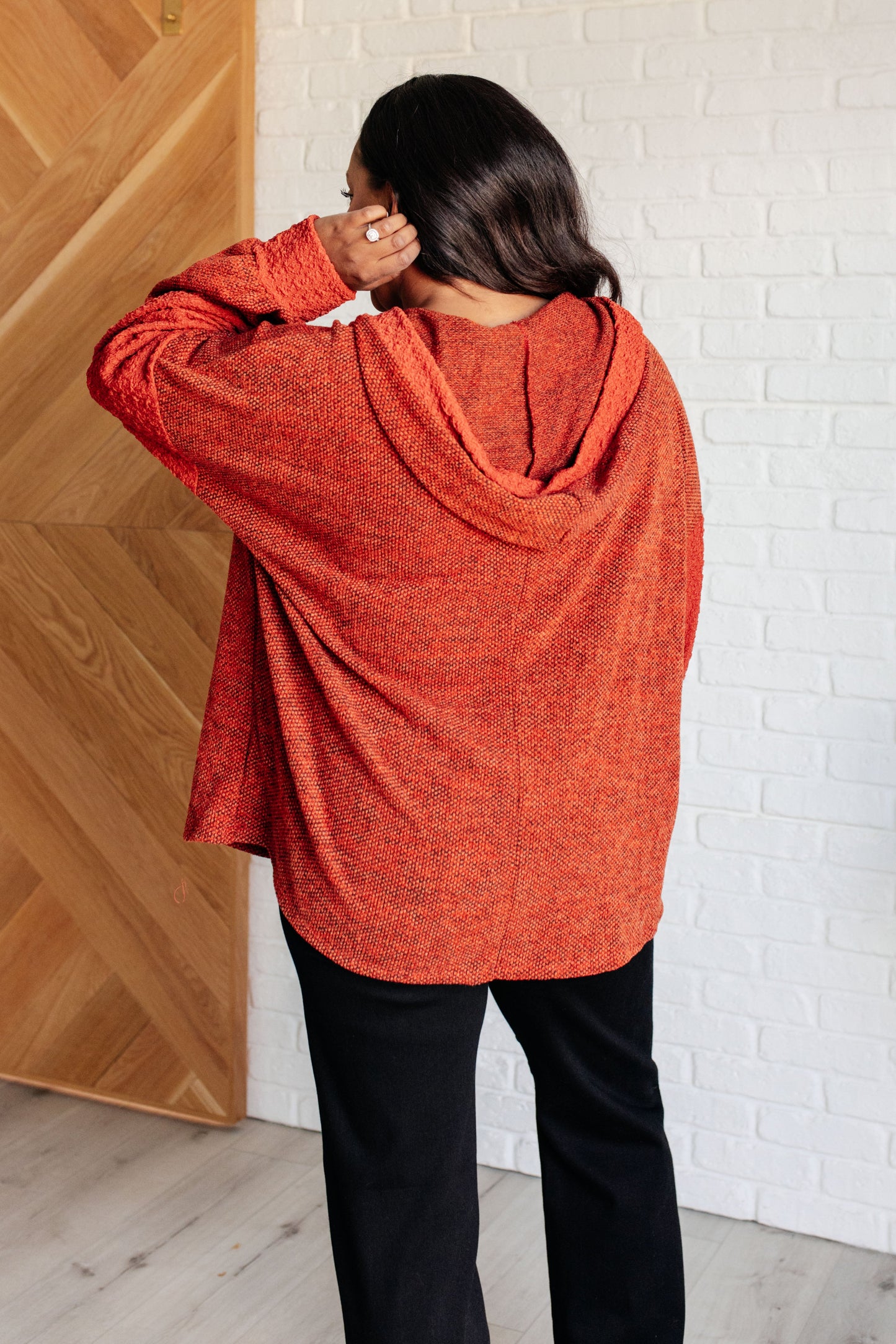 Person wearing an orange hoodie standing against a white brick wall.