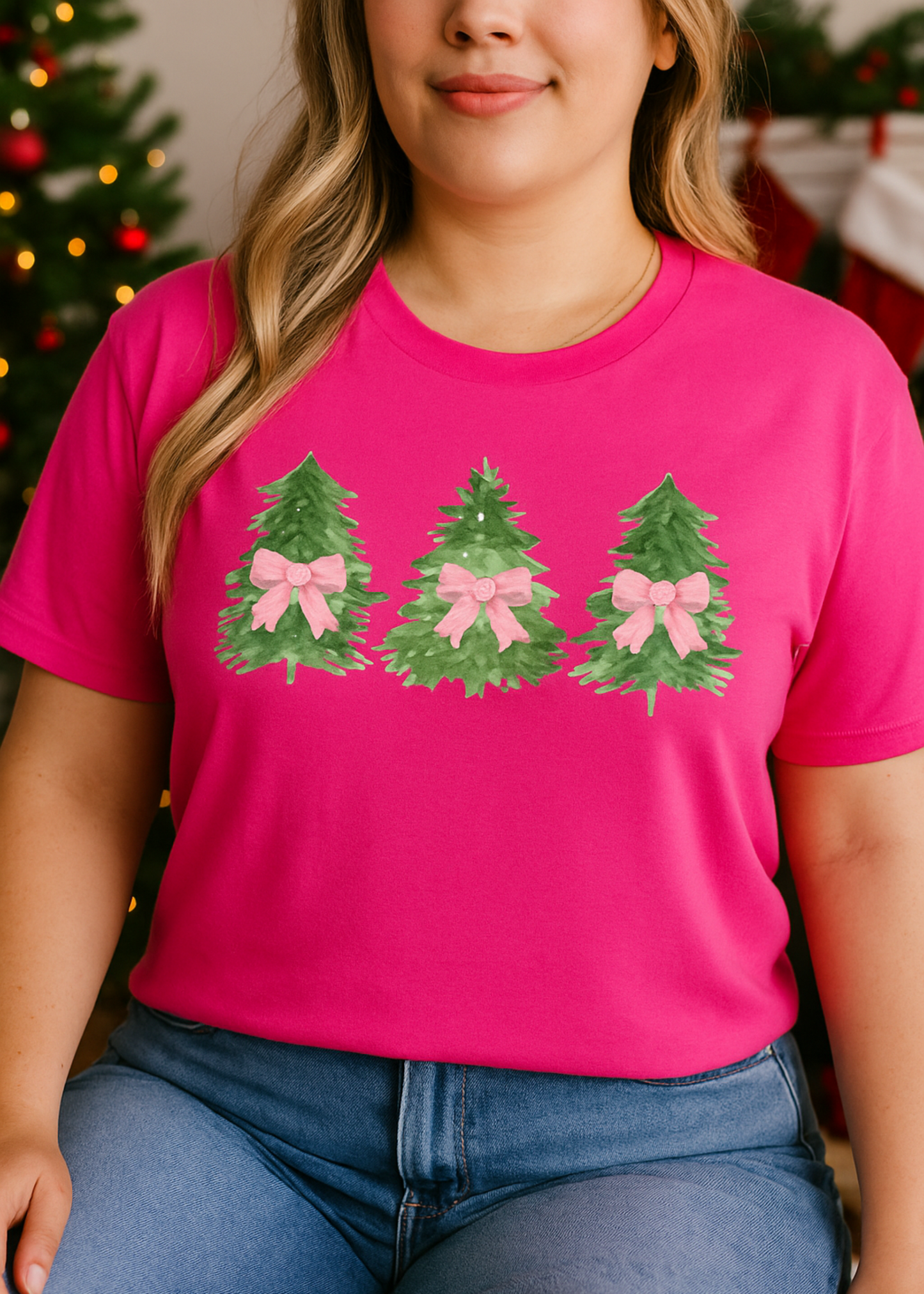 Person wearing a pink t-shirt with Christmas tree designs and pink bows, standing in front of a decorated Christmas tree.