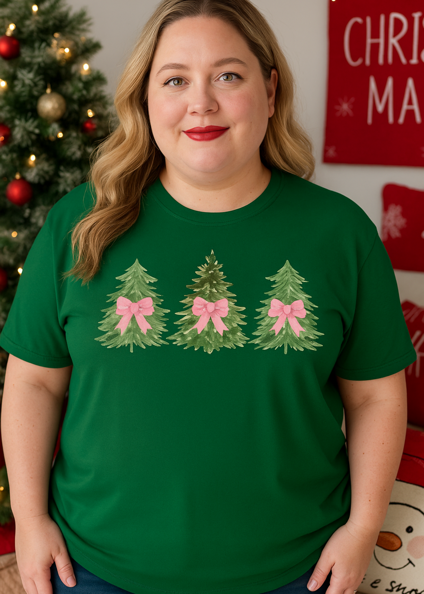 Woman wearing a green t-shirt with Christmas tree designs and bows in front of a decorated Christmas tree.