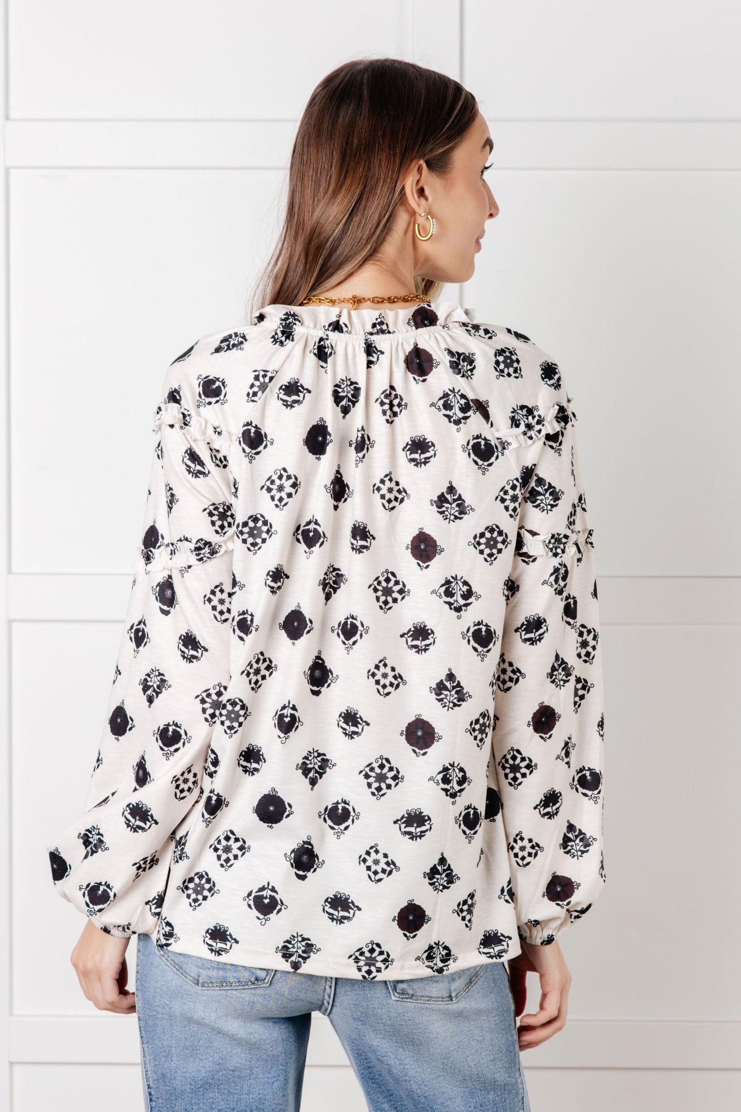 Woman wearing a white blouse with black floral pattern against a white wall.