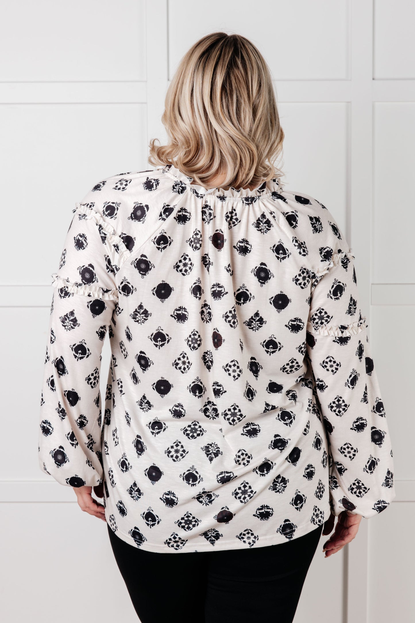 Person wearing a black and white floral blouse against a white tiled wall.