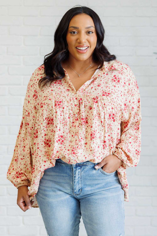 Woman wearing a floral blouse and jeans against a white brick wall