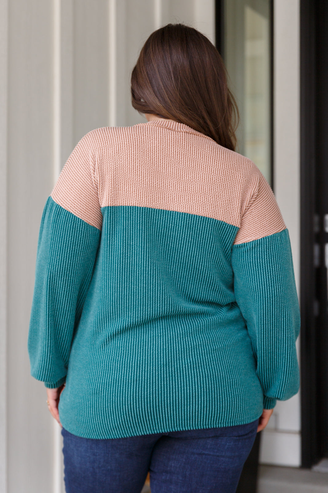 Person wearing a teal and beige sweater standing in front of a door.