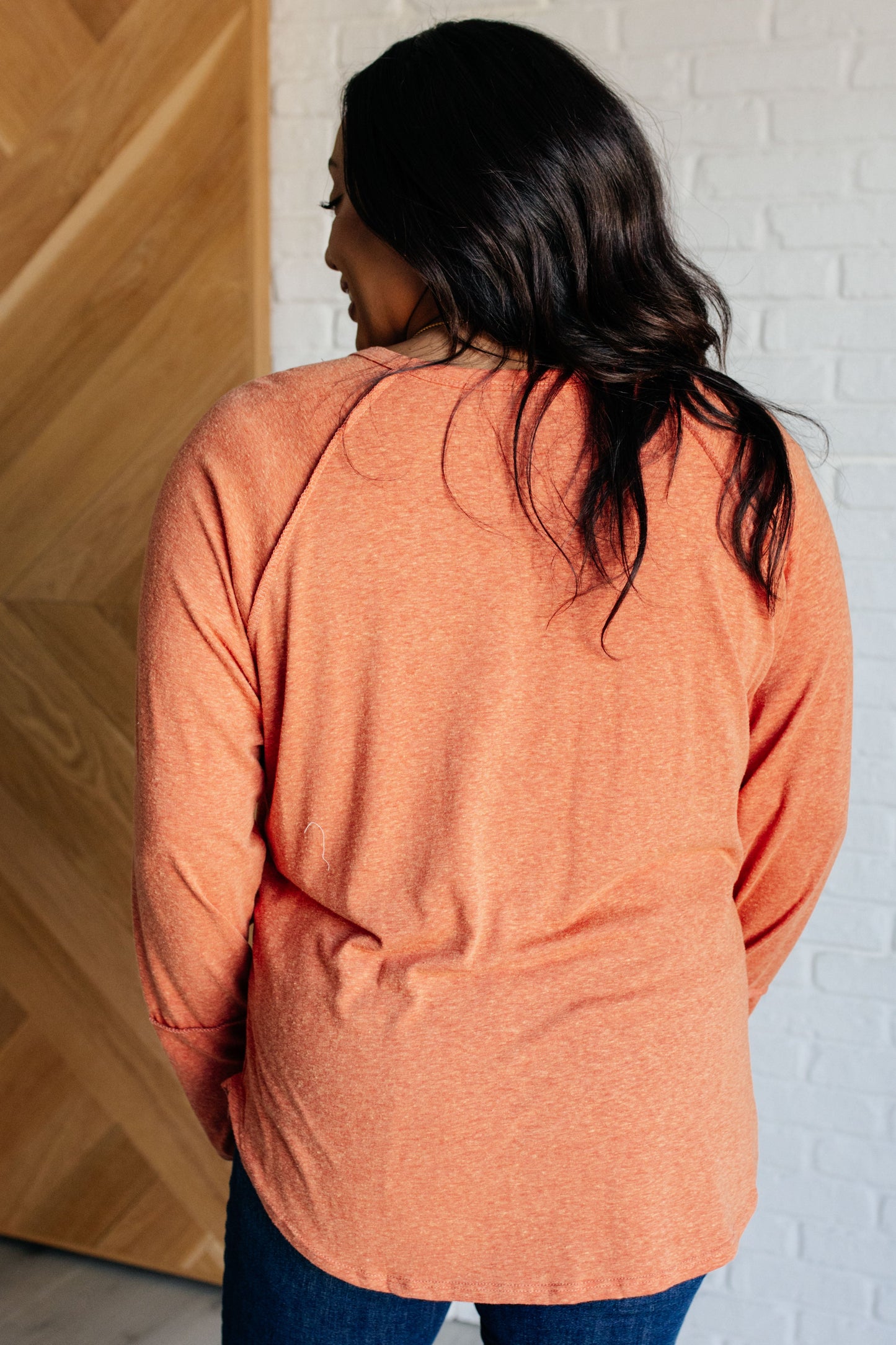 Person wearing an orange sweater with a white brick wall background