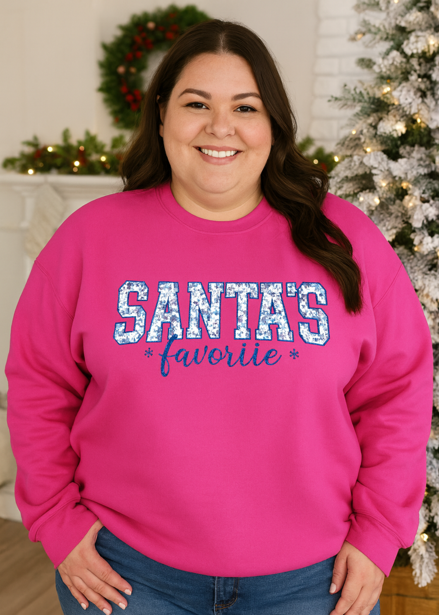 Person wearing a pink sweatshirt with 'Santa's Favorite' text in front of a decorated Christmas tree.