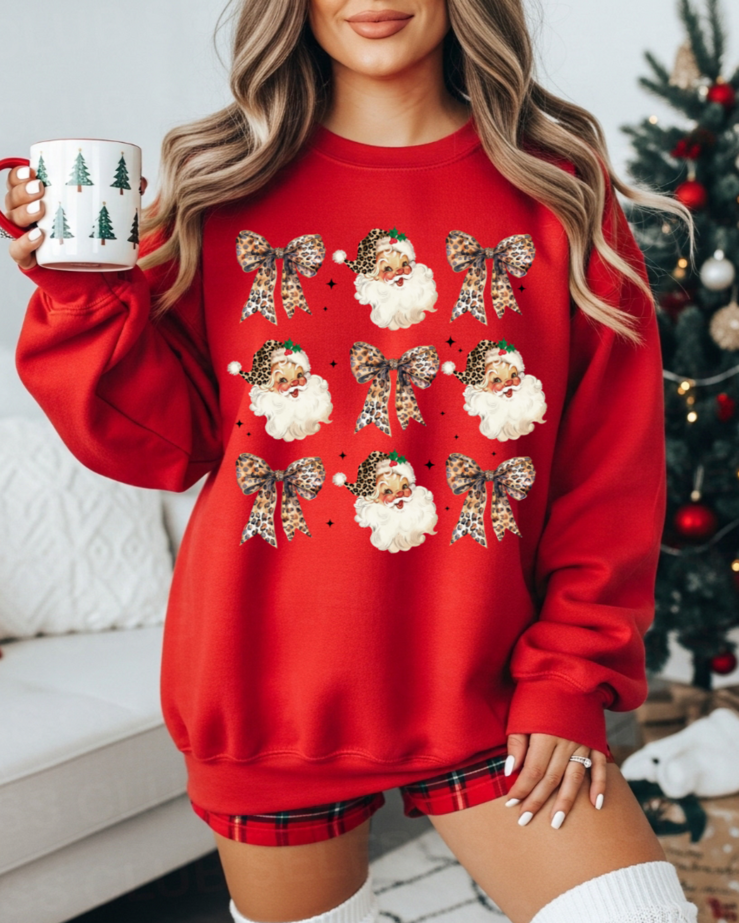 Person wearing a red Christmas-themed sweatshirt with Santa Claus and bows, holding a mug in a festive setting.