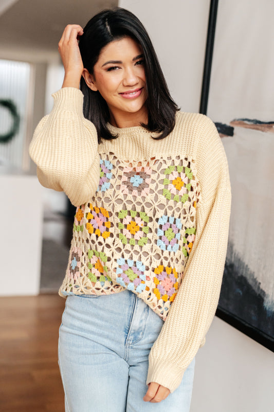 Woman wearing a beige sweater with a colorful floral pattern over a plain top.