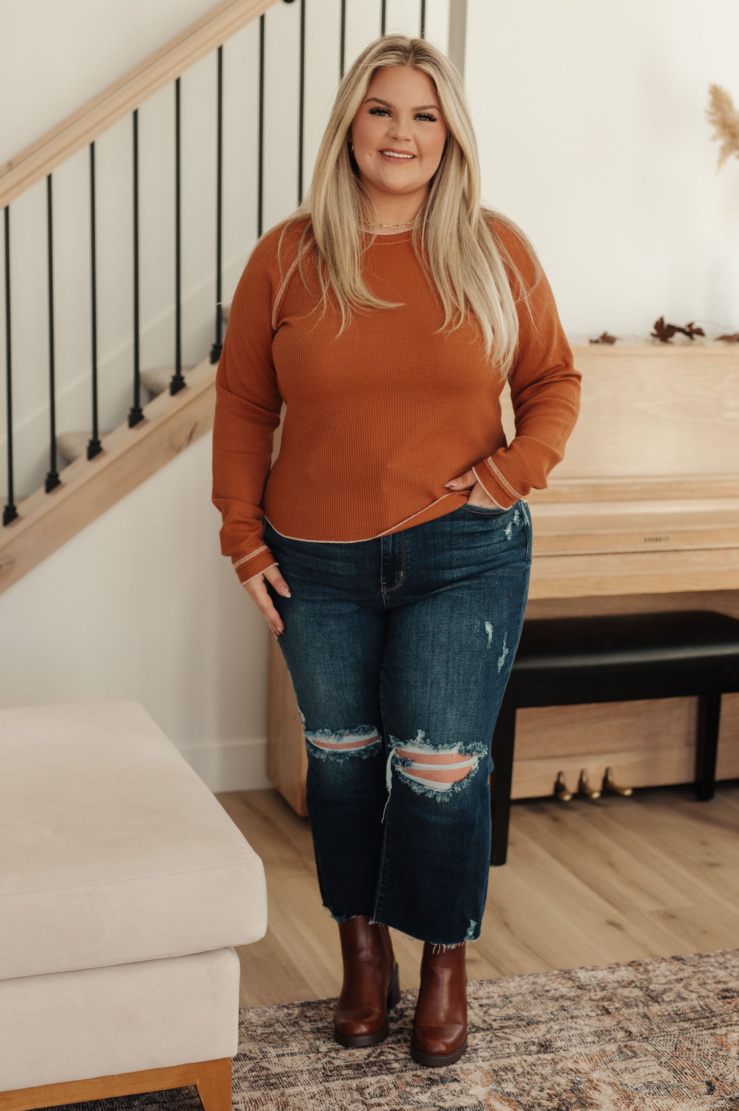 Woman wearing an orange sweater and blue jeans standing in a home setting.