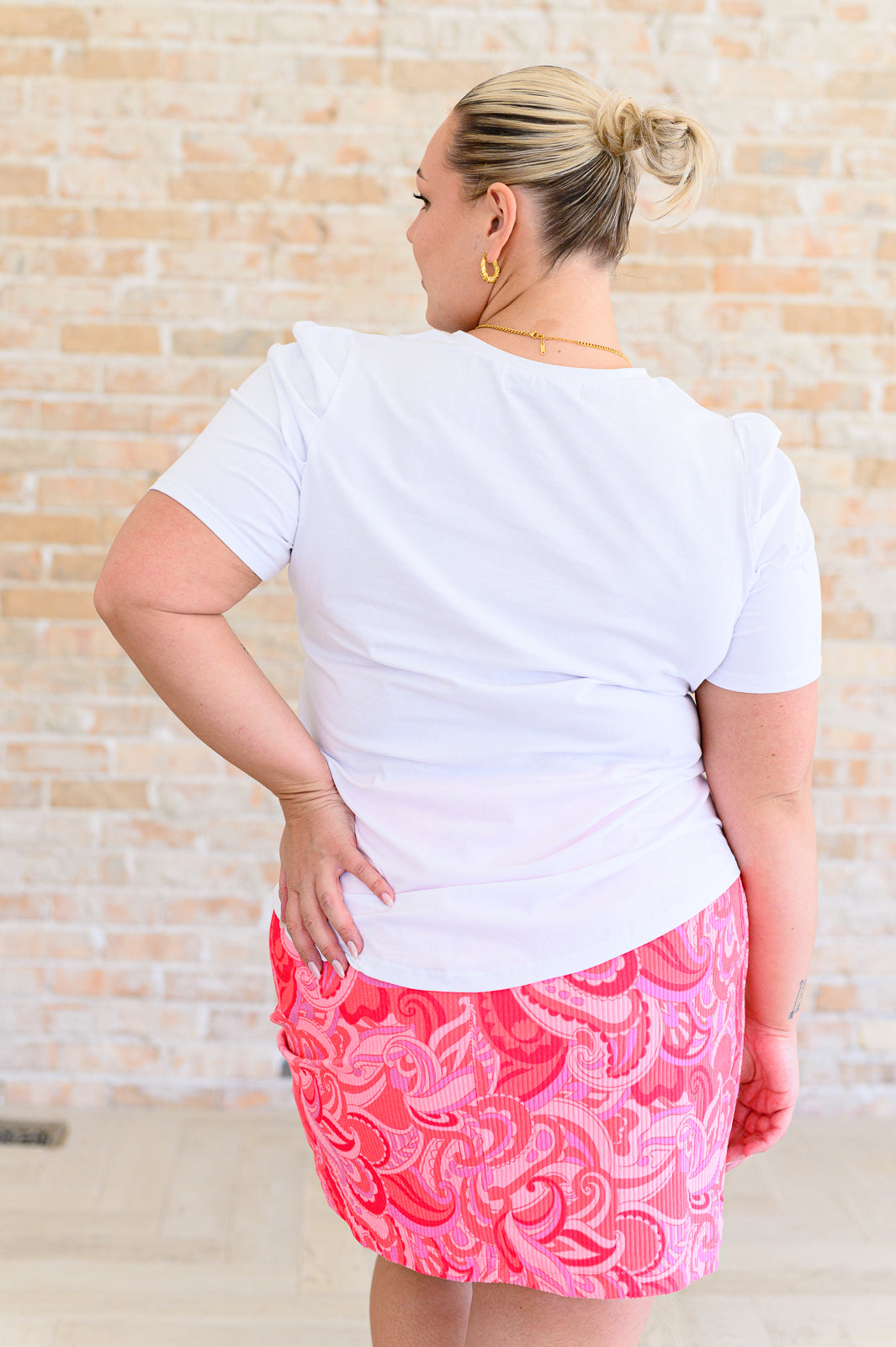 A woman wearing a white v-neck tee shirt and a pink paisley mini skirt.