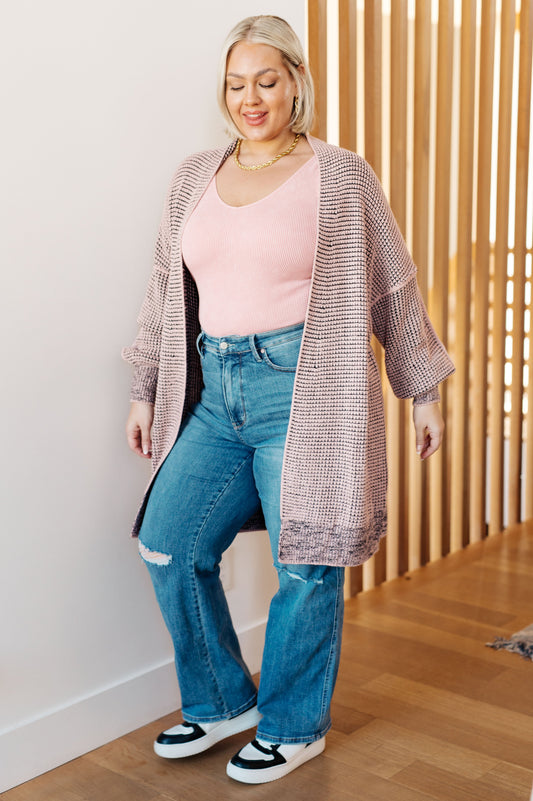 Woman wearing a pink top, blue jeans, and a patterned cardigan indoors.