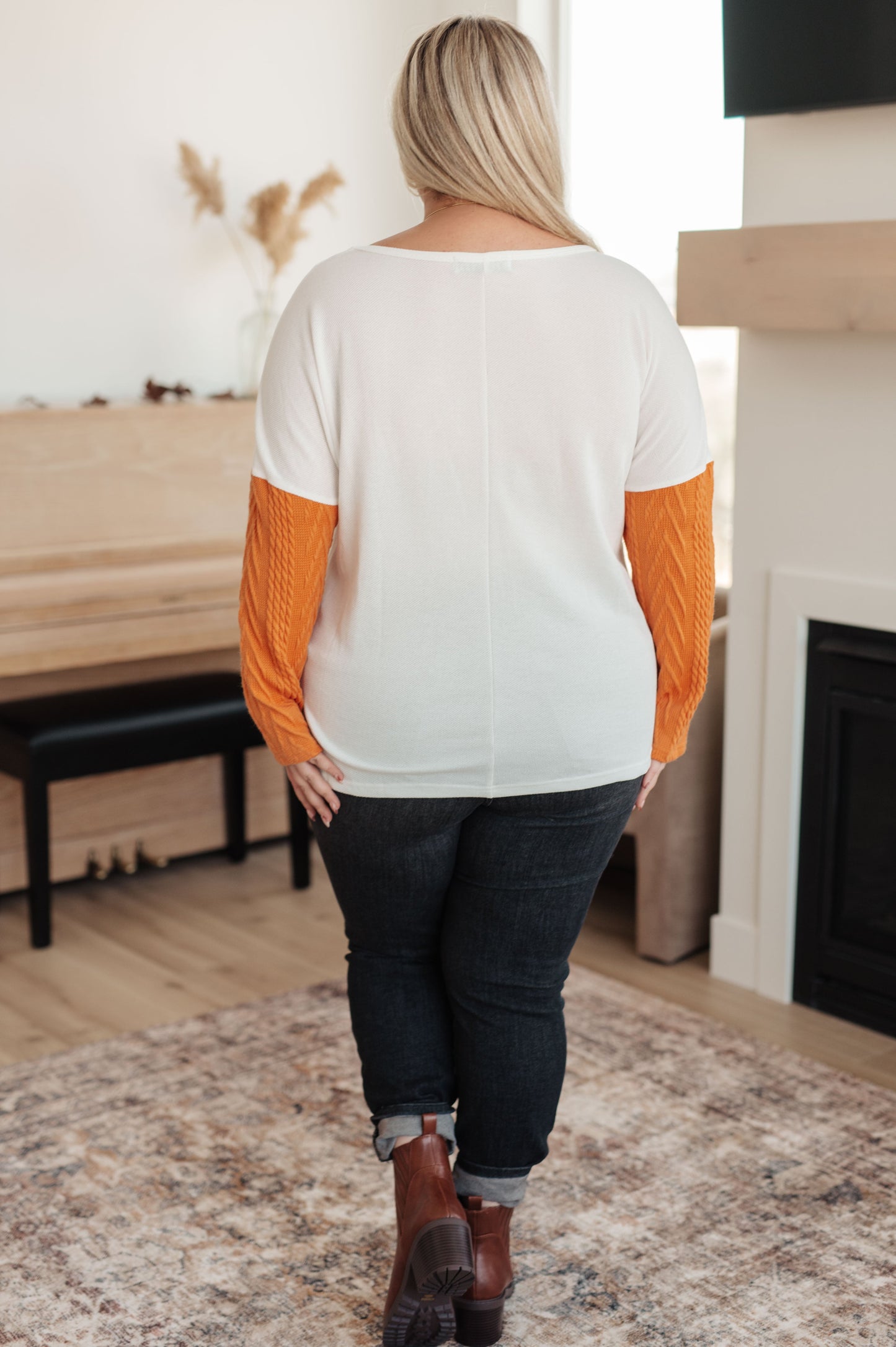Person wearing a white and orange sweater in a room with a fireplace and wooden bench.