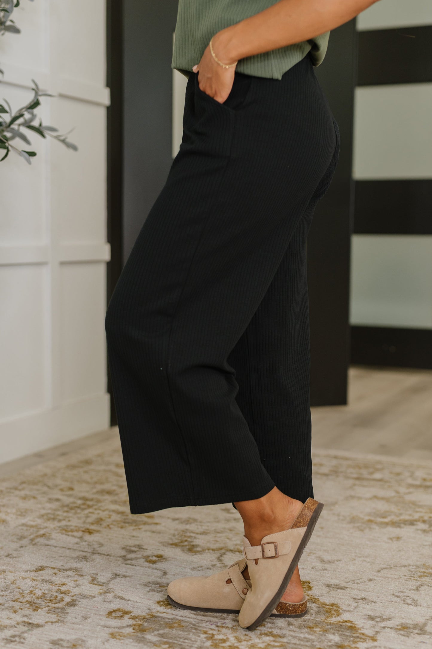 Person wearing black pants and beige sandals standing on a patterned rug.