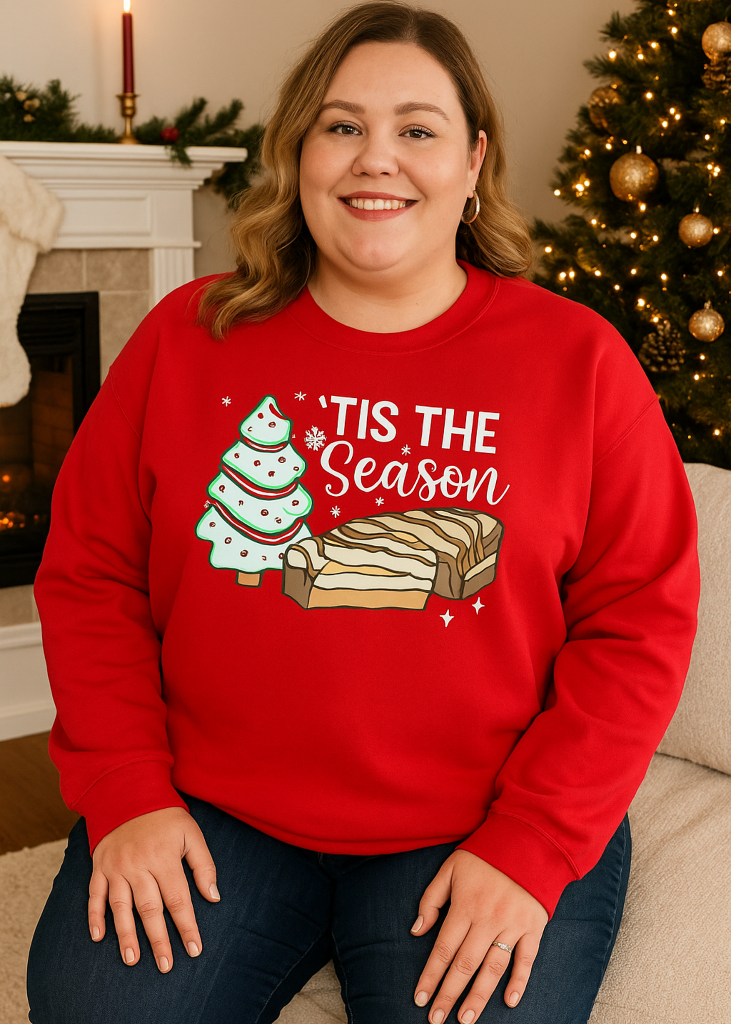 Person wearing a red sweatshirt with Christmas-themed design sitting in front of a decorated fireplace and tree.