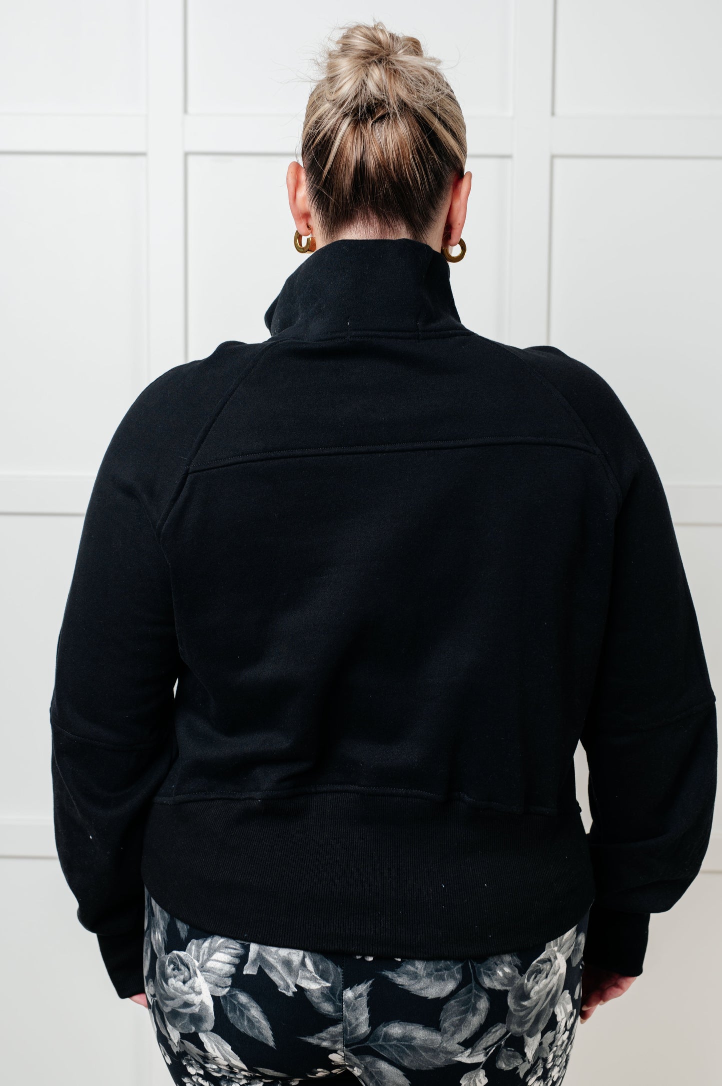 Person wearing a black jacket with a white tiled wall background