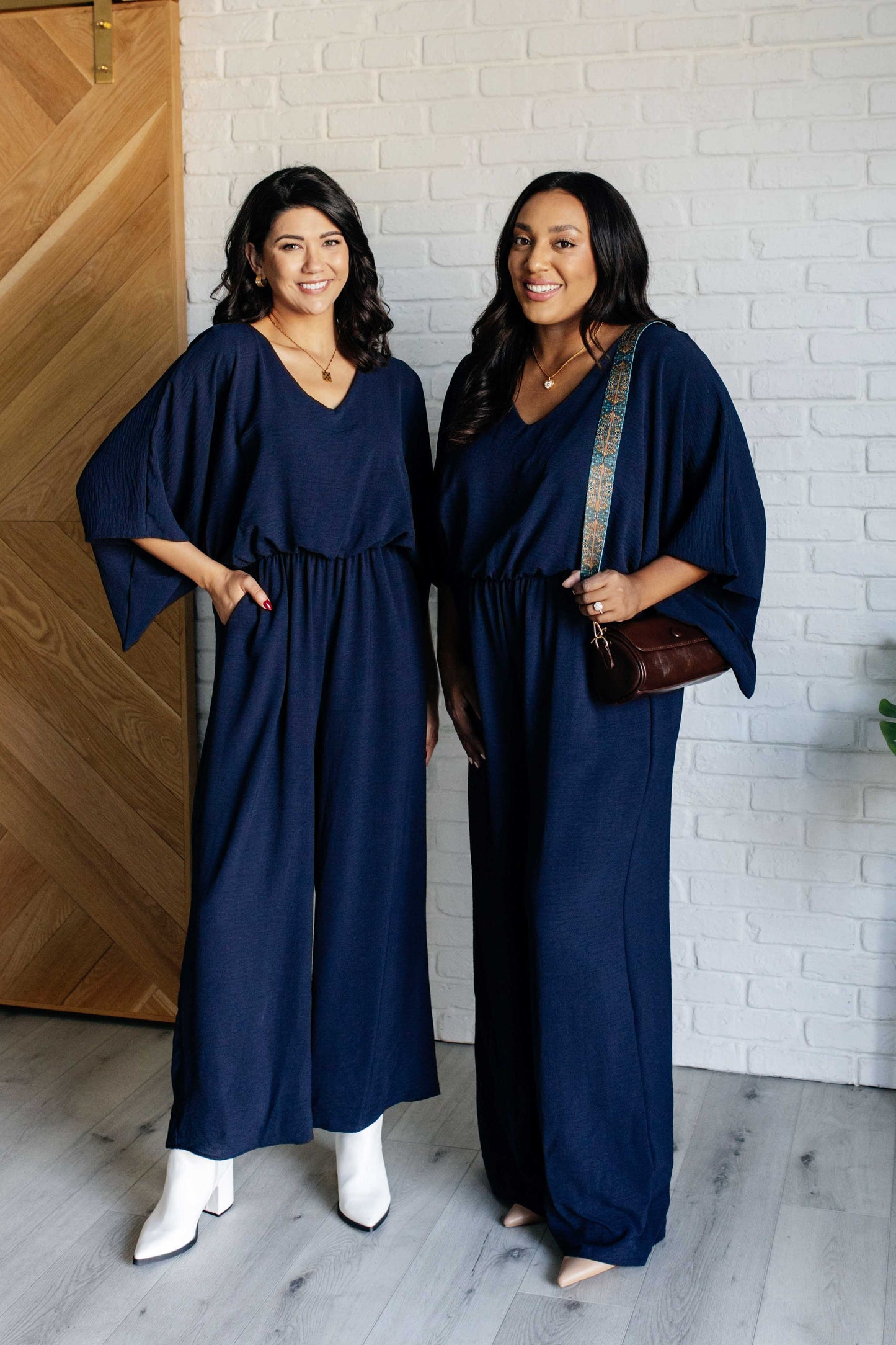 Two women wearing navy blue dresses standing in front of a white brick wall.