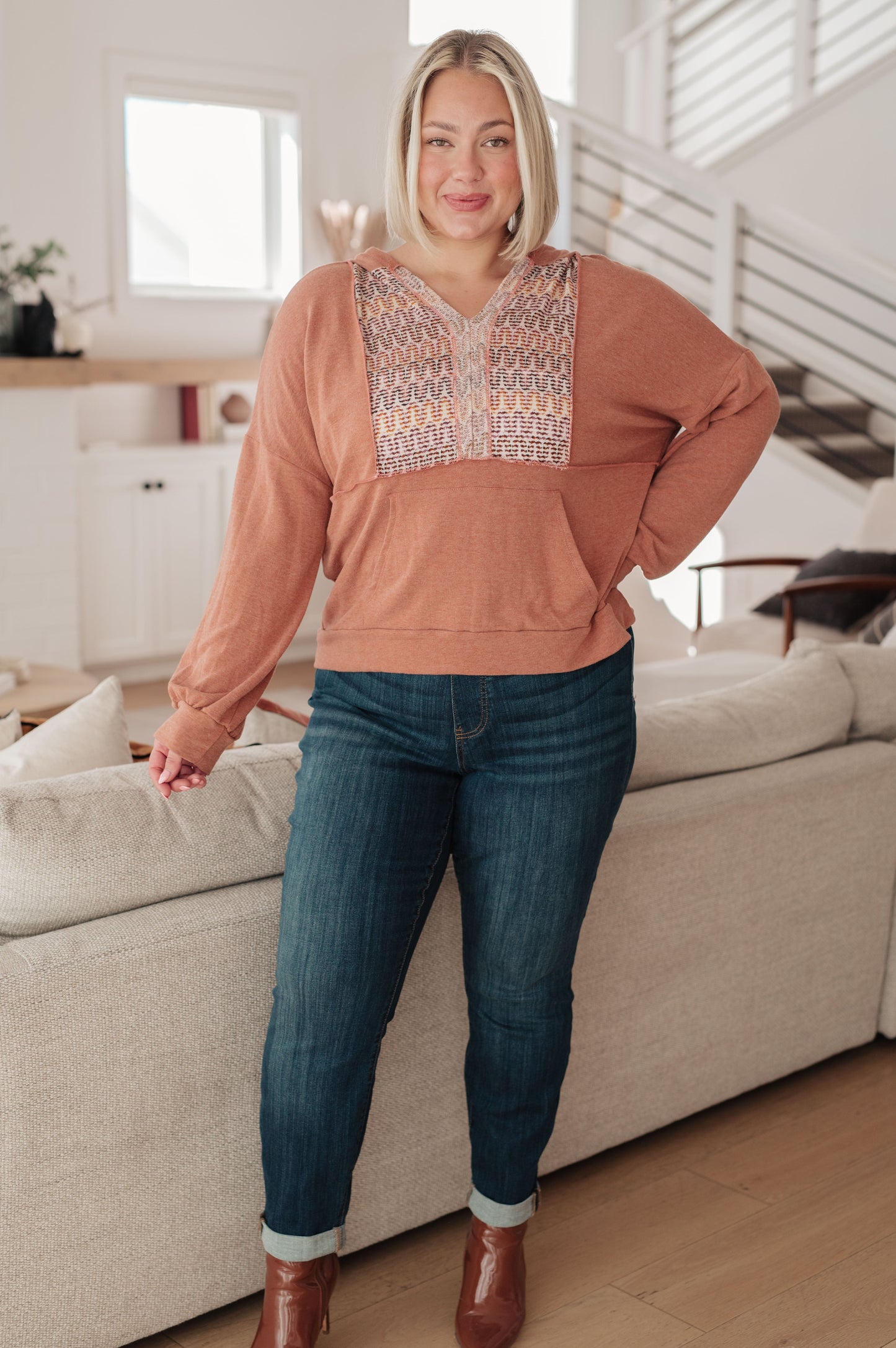 Woman wearing a peach blouse with patterned accents and blue jeans in a living room.