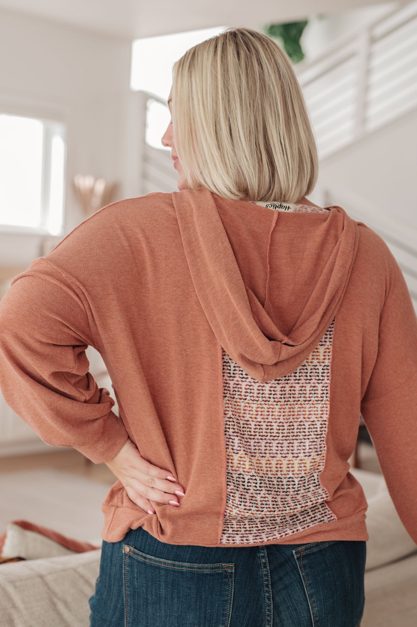 Person wearing a brown hoodie with a patterned back in a room.
