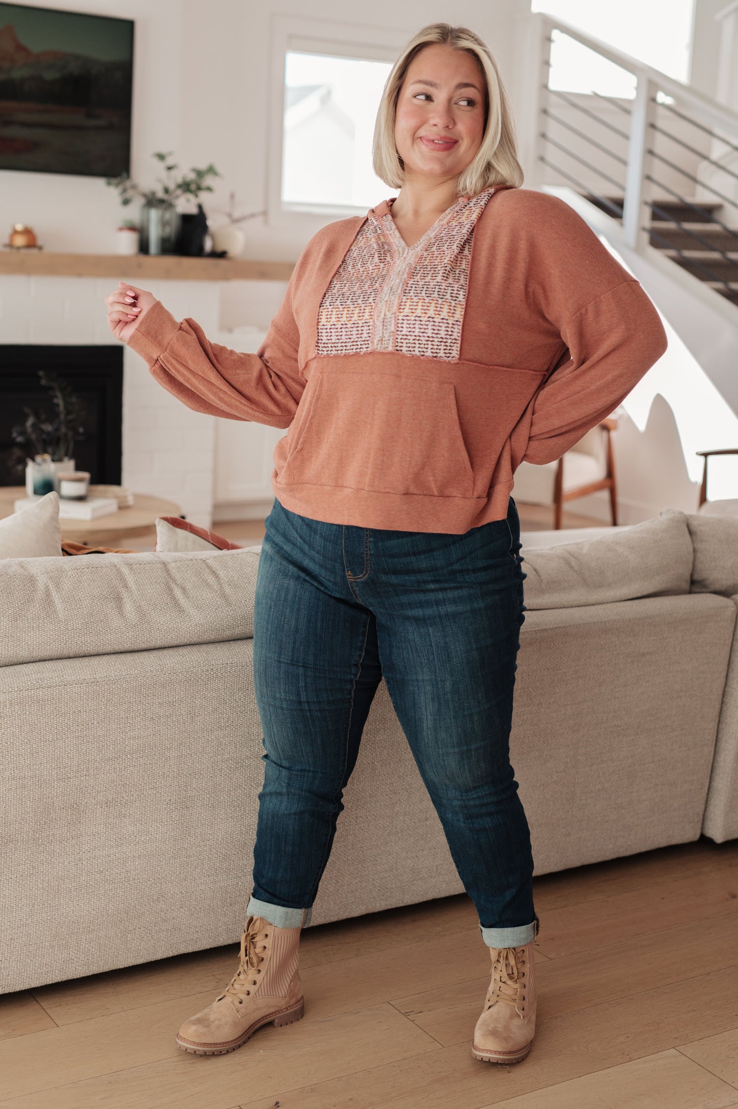 Woman wearing a brown top with lace details and blue jeans in a living room.