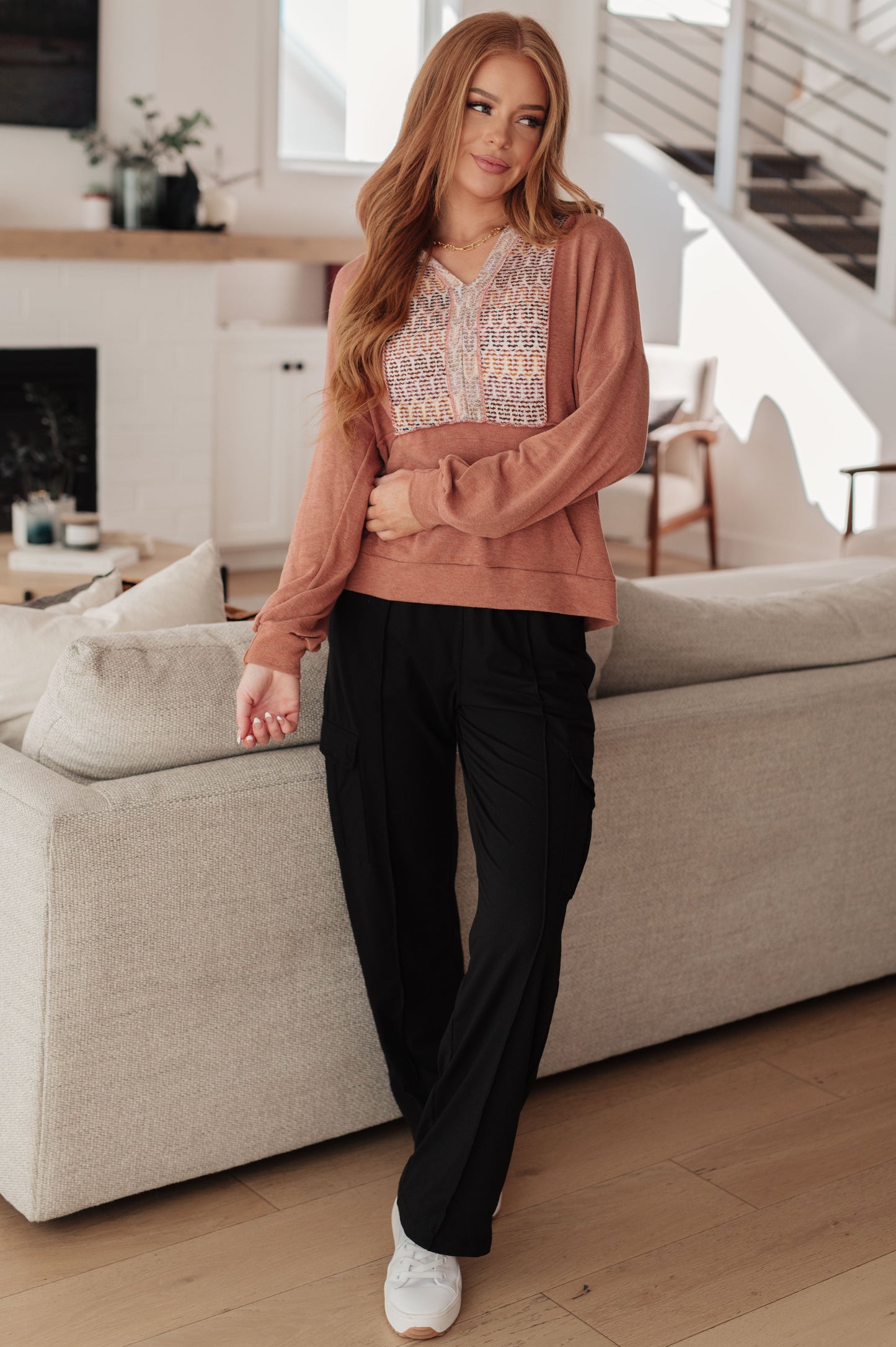 Woman in a living room wearing a pink cardigan and black pants.