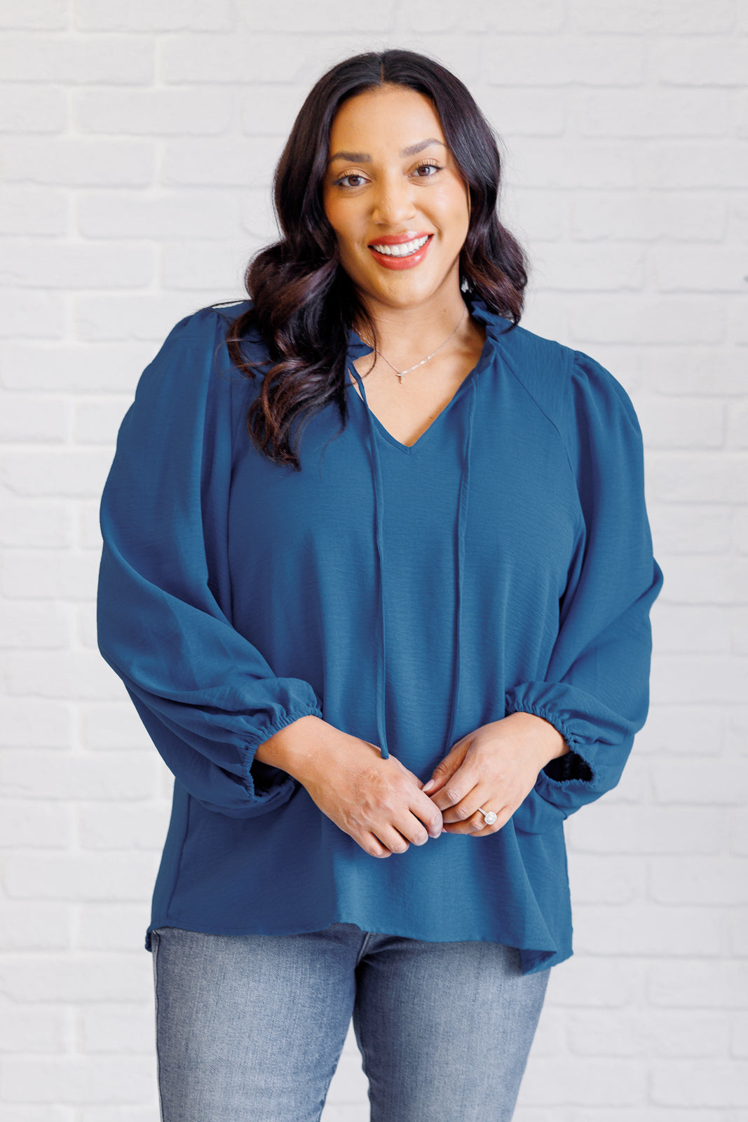 Woman wearing a blue blouse against a white brick wall