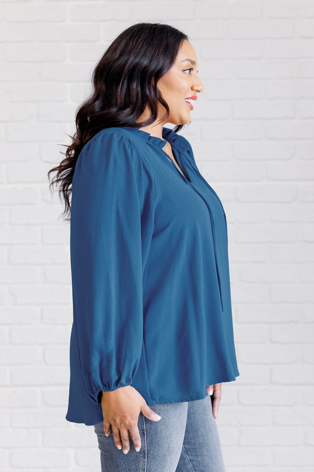 Woman wearing a teal blouse against a white brick wall