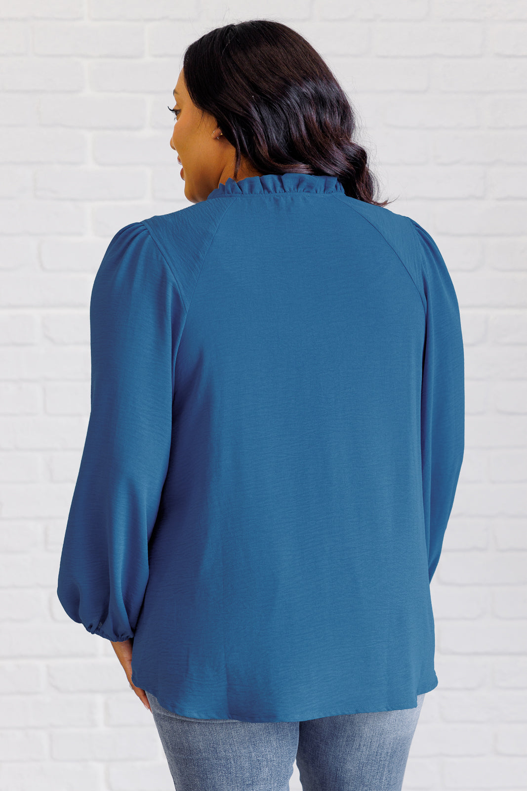 Woman wearing a blue blouse against a white brick wall