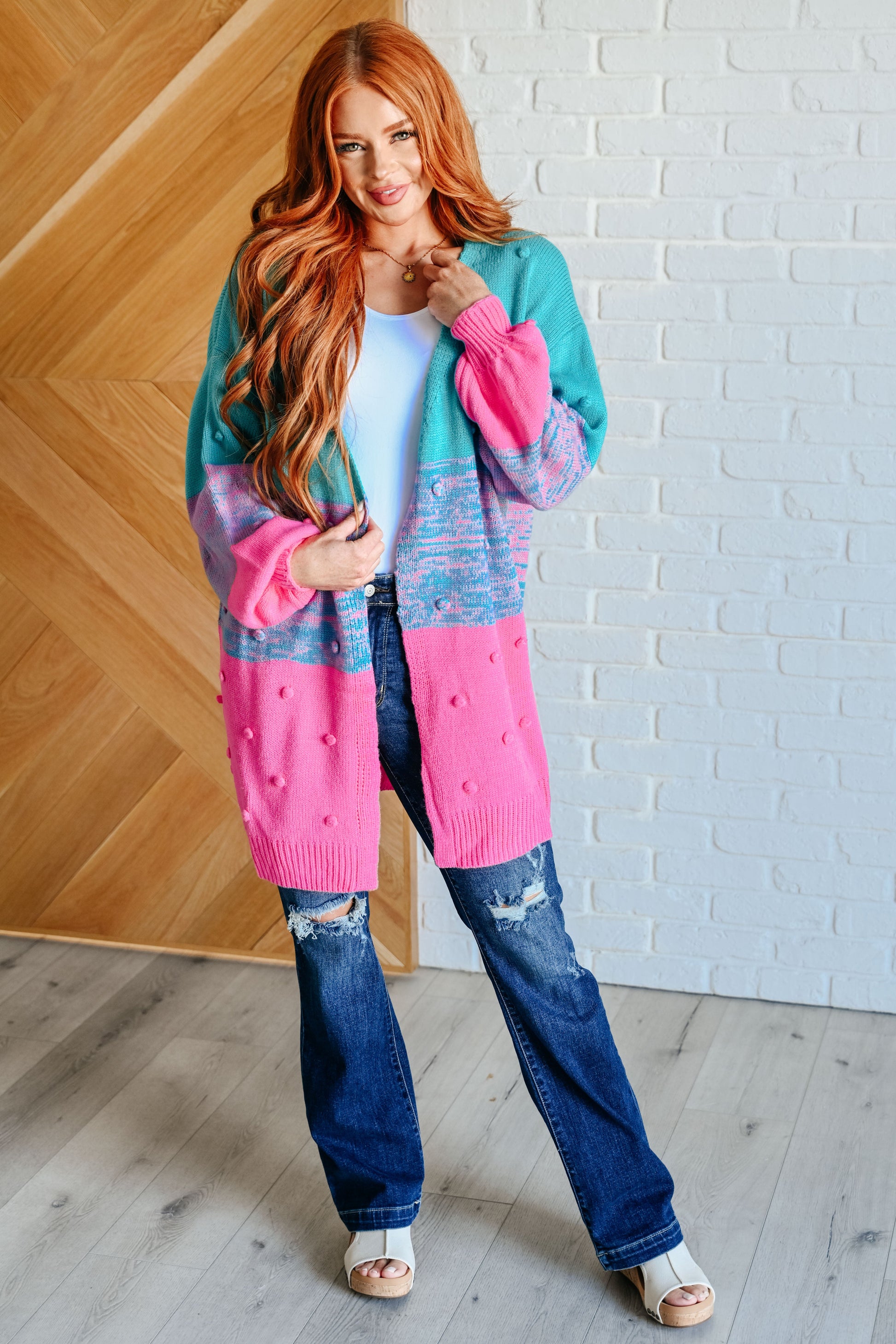 Woman wearing a colorful cardigan with a white brick wall background
