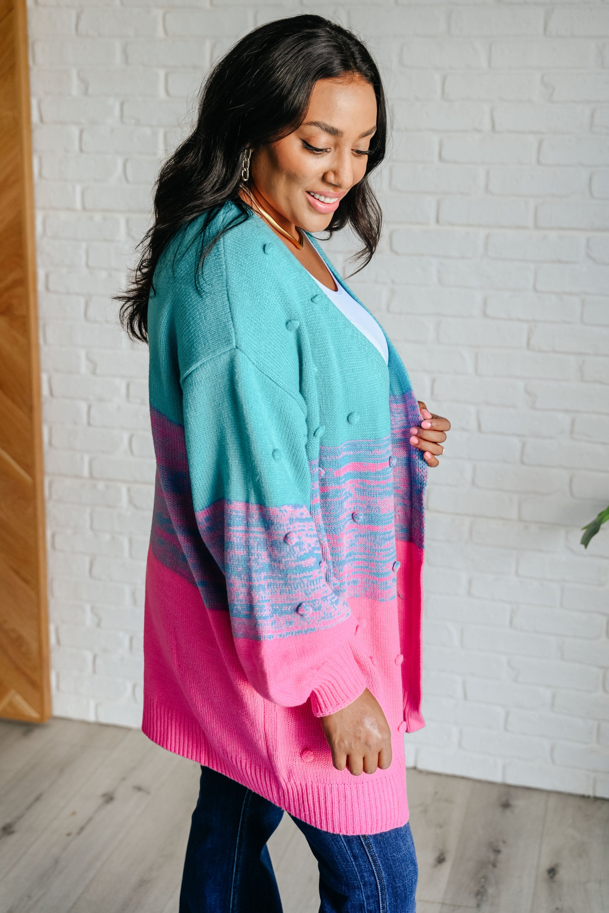Woman wearing a colorful cardigan in front of a white brick wall.