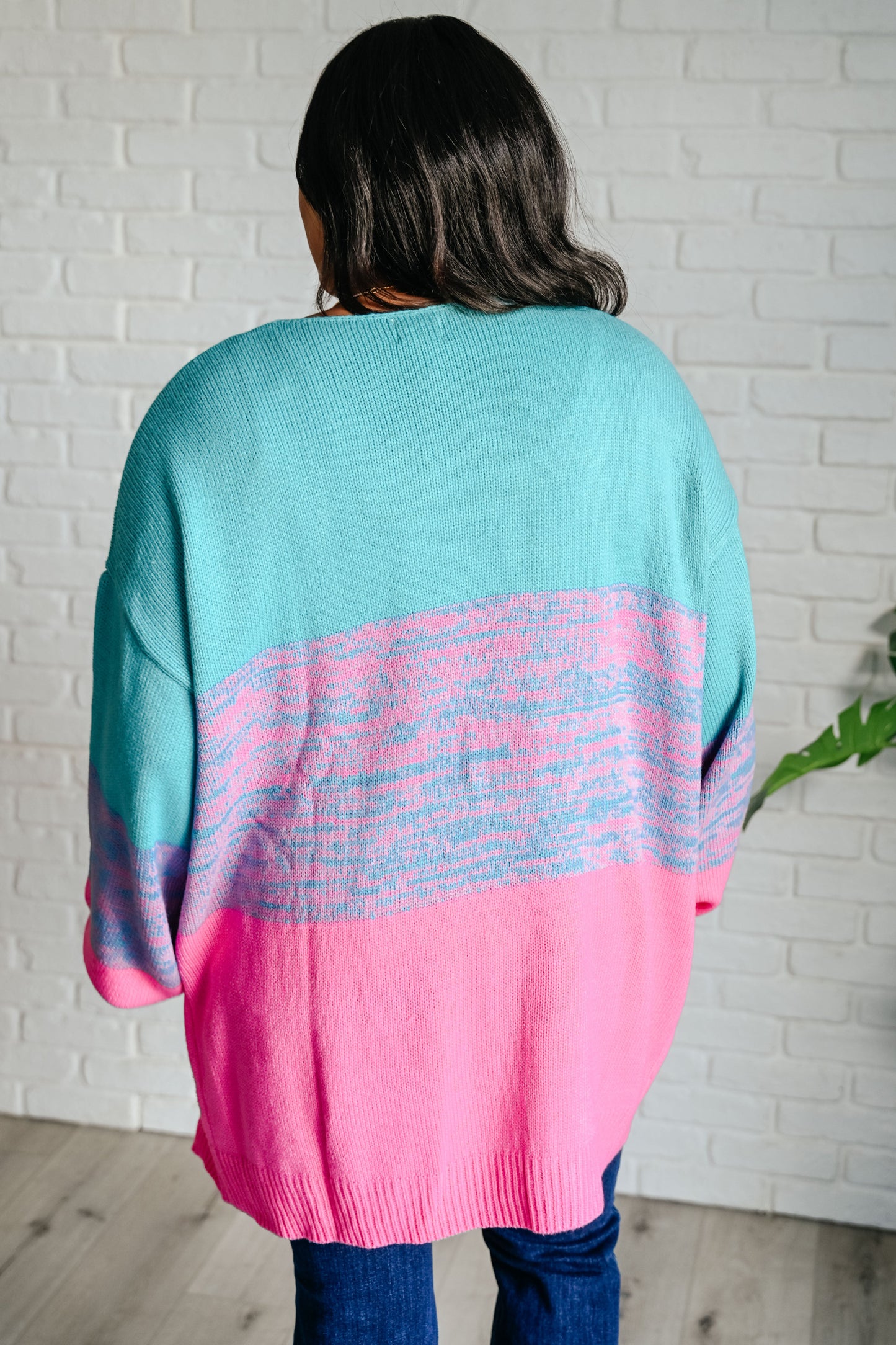 Person wearing a colorful sweater with a white brick wall background