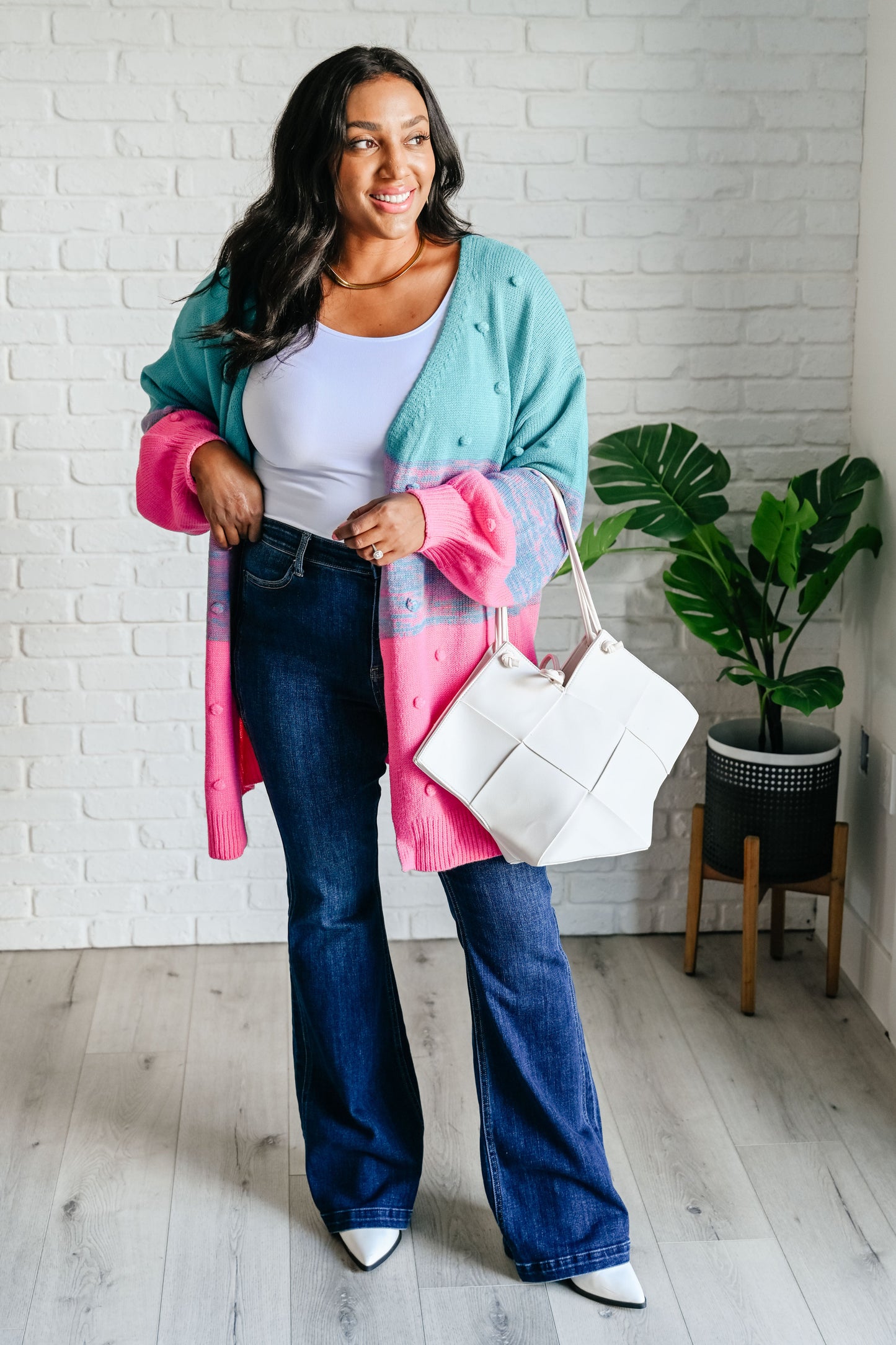 Woman wearing a colorful outfit with a white bag indoors.