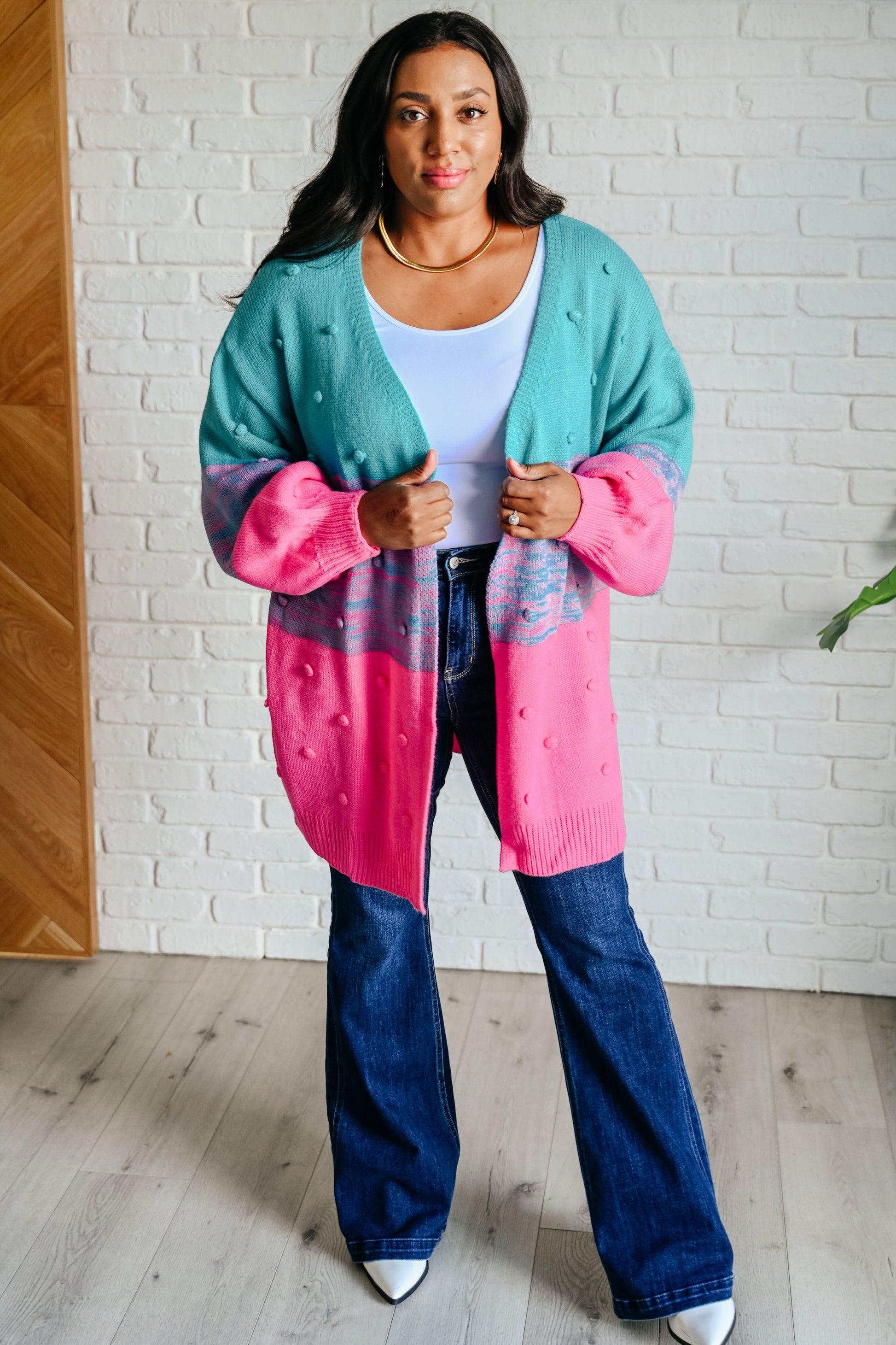 Woman wearing a colorful cardigan with a white brick wall background
