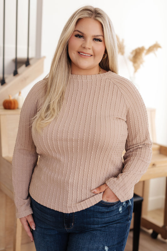 Woman wearing a beige ribbed sweater and blue jeans indoors.