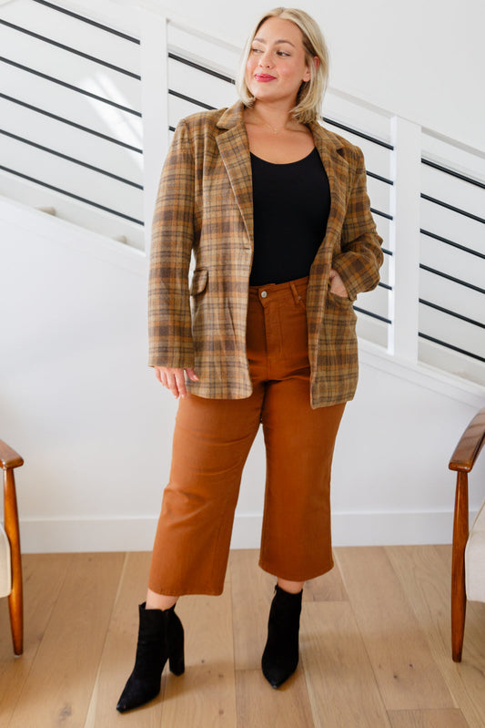 Woman wearing a plaid blazer, black top, and brown pants indoors.