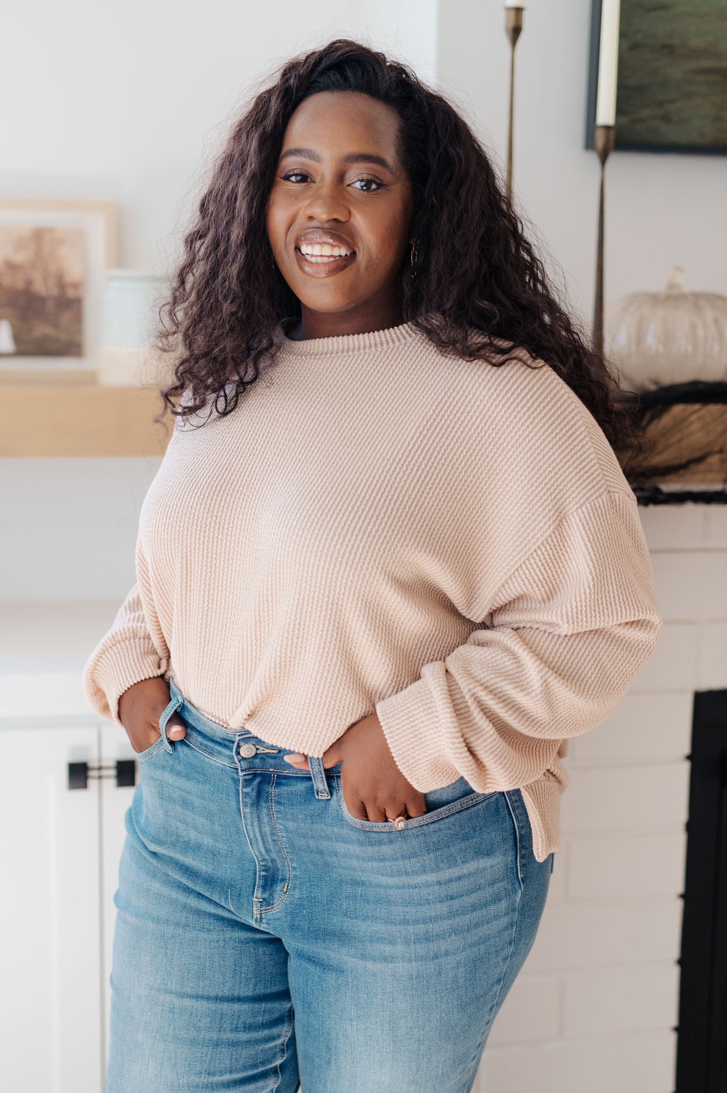 Woman wearing a beige sweater and blue jeans indoors