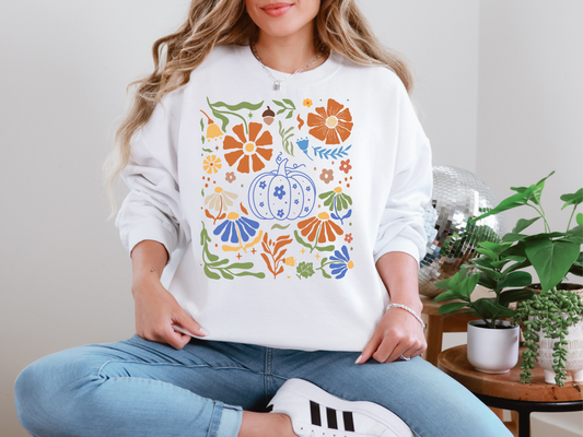 Person wearing a white sweatshirt with colorful pumpkin design sitting in a room with plants.