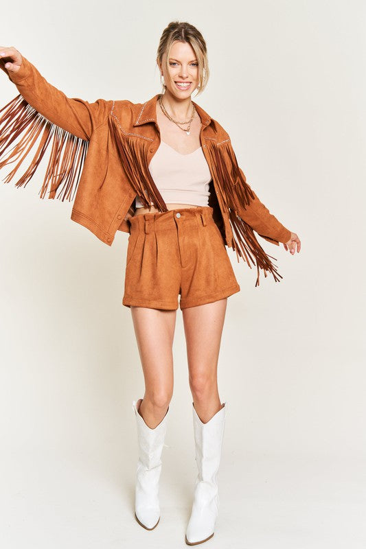 Woman wearing a brown fringe jacket, shorts, and white boots on a beige background